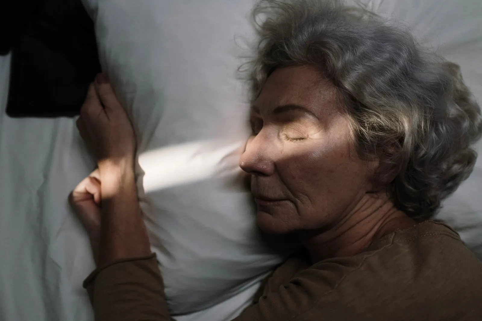 Older woman resting peacefully on a pillow with sunlight on her face