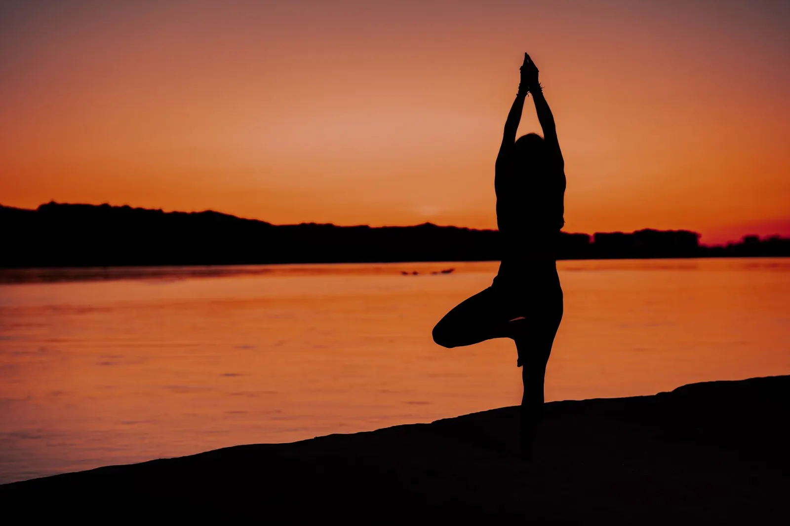 Silhouette of a woman in a yoga pose by the water at sunset