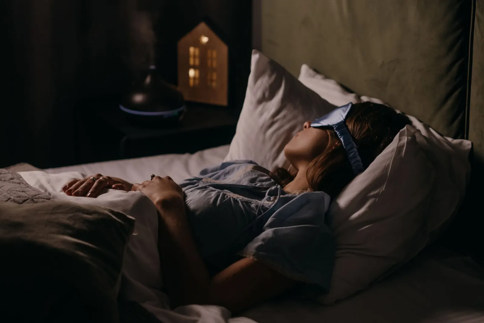 Woman sleeping in an eye mask in a dim bedroom