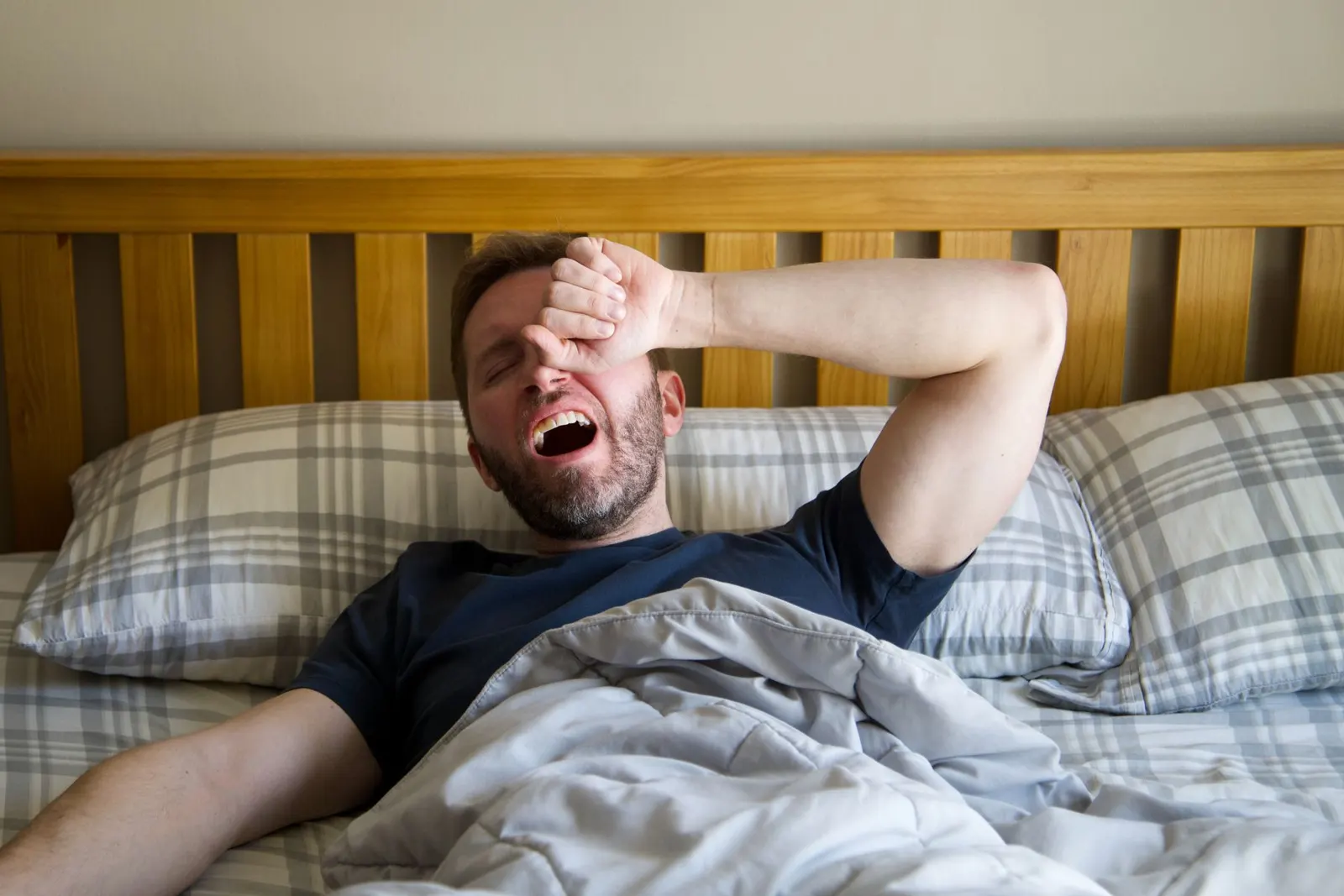Man yawning as he wakes up in bed in morning light
